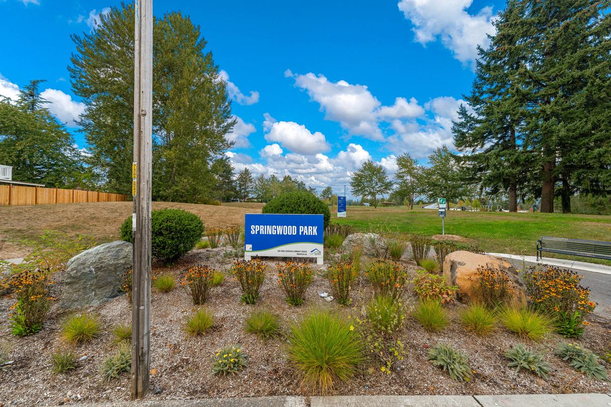 Entrance sign for Springwood Park with landscaped plantings, open lawn, and tall evergreen trees